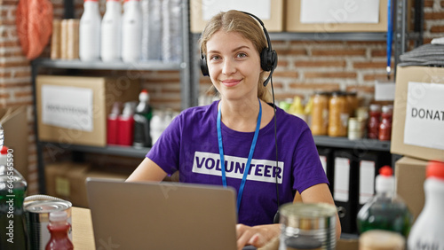 Young blonde woman volunteer using laptop and headphones smiling at charity center