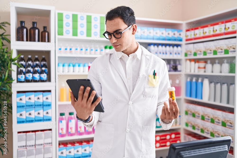 Young hispanic man pharmacist using touchpad holding pills bottle at pharmacy Young hispanic man pharmacist using touchpad holding pills bottle at pharmacy