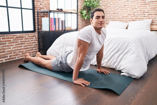 Young hispanic man stretching back sitting on floor at bedroom