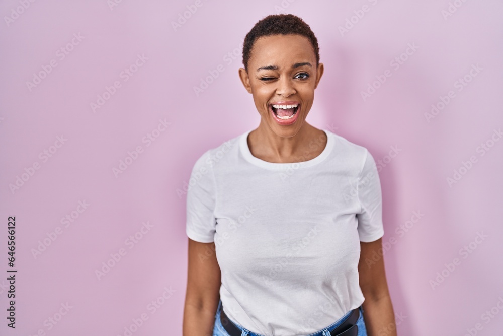 Beautiful african american woman standing over pink background winking looking at the camera with sexy expression, cheerful and happy face.