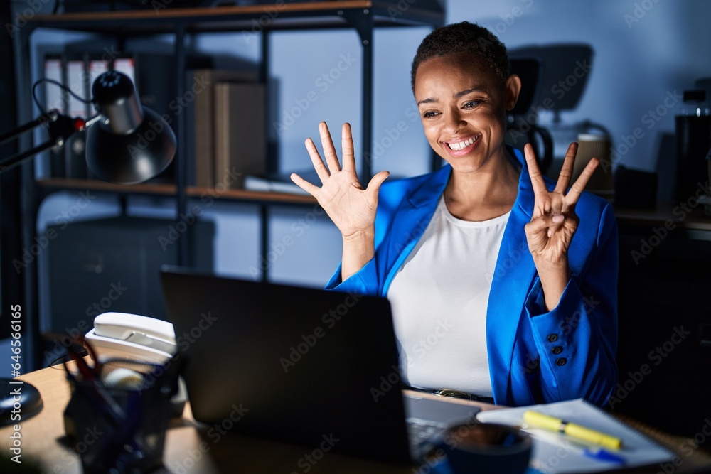 Beautiful african american woman working at the office at night showing and pointing up with fingers number eight while smiling confident and happy. Beautiful african american woman working at the office at night showing and pointing up with fingers number eight while smiling confident and happy.
