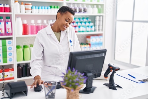 African american woman pharmacist talking on telephone using computer at pharmacy