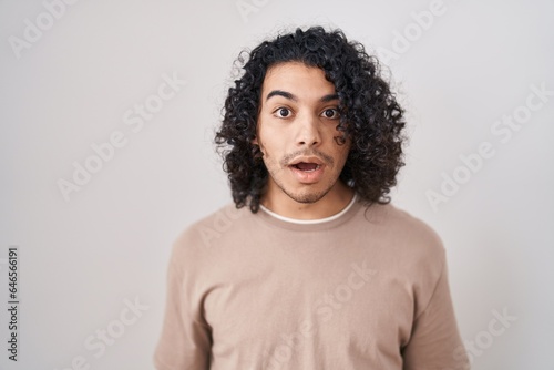 Hispanic man with curly hair standing over white background afraid and shocked with surprise and amazed expression, fear and excited face.