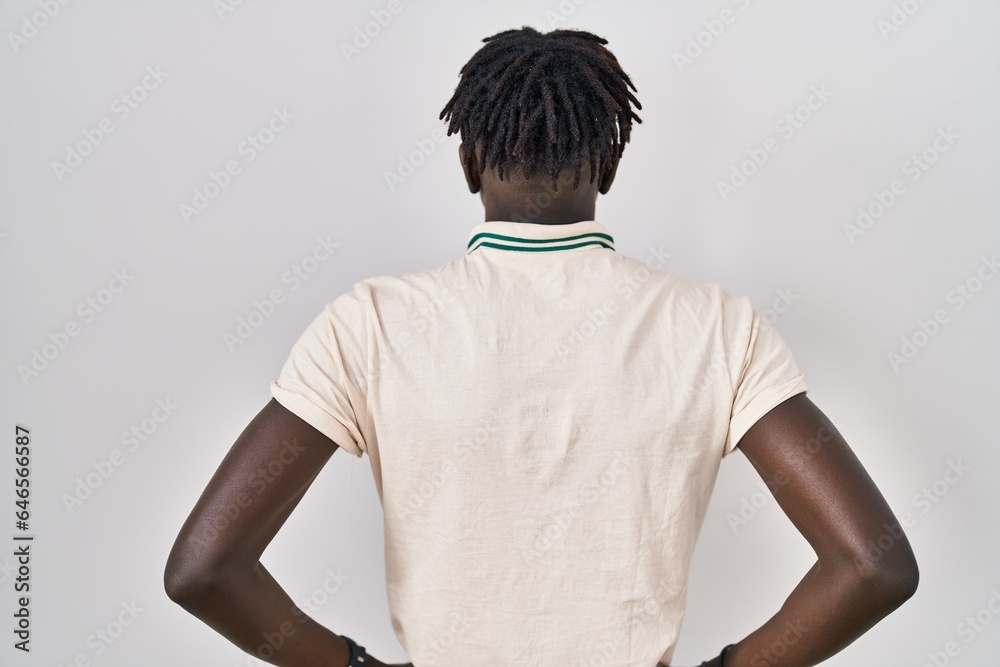African man with dreadlocks standing over isolated background standing backwards looking away with arms on body African man with dreadlocks standing over isolated background standing backwards looking away with arms on body