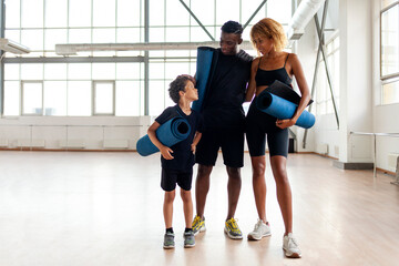 african american young family standing together in the gym and holding yoga mat, father mom and son on fitness training