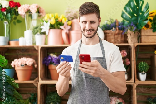 Young caucasian man florist using smartphone and credit card at flower shop