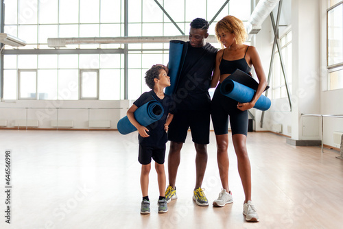 african american young family standing together in the gym and holding yoga mat, father mom and son on fitness training