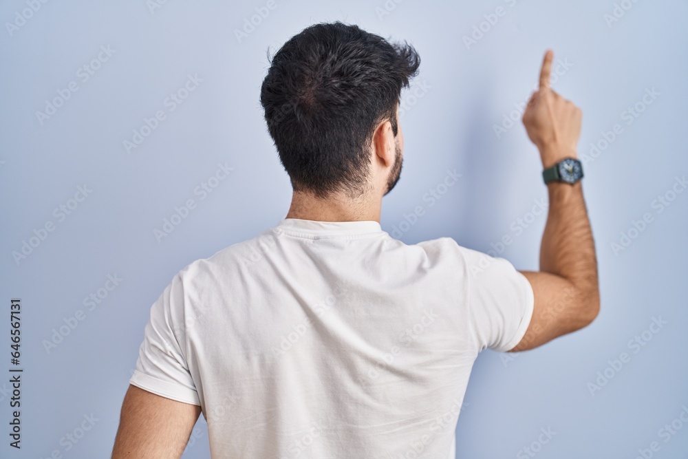 Hispanic man with beard standing over white background posing backwards pointing ahead with finger hand Hispanic man with beard standing over white background posing backwards pointing ahead with finger hand