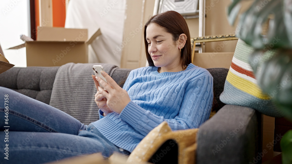 Young caucasian woman using smartphone sitting on sofa at new home Young caucasian woman using smartphone sitting on sofa at new home