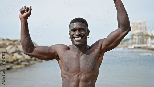 African american man tourist smiling confident standing shirtless dancing at the beach