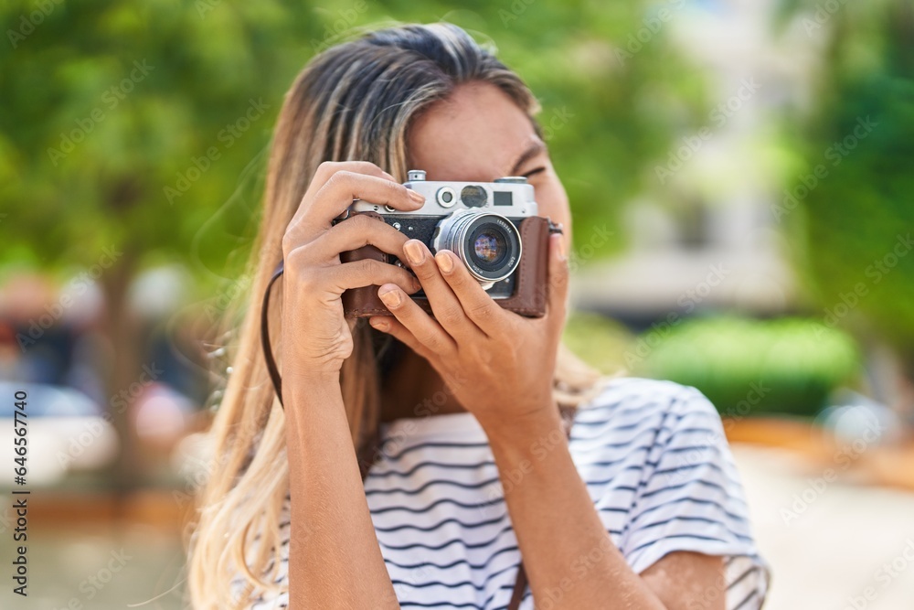 Young blonde woman smiling confident using vintage camera at park
