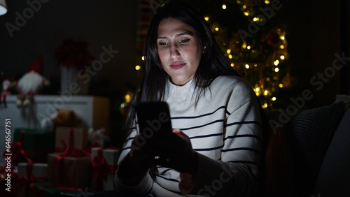 Young beautiful hispanic woman using smartphone celebrating christmas at home