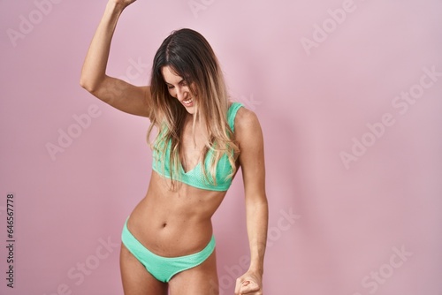Young hispanic woman wearing bikini over pink background dancing happy and cheerful, smiling moving casual and confident listening to music © Krakenimages.com