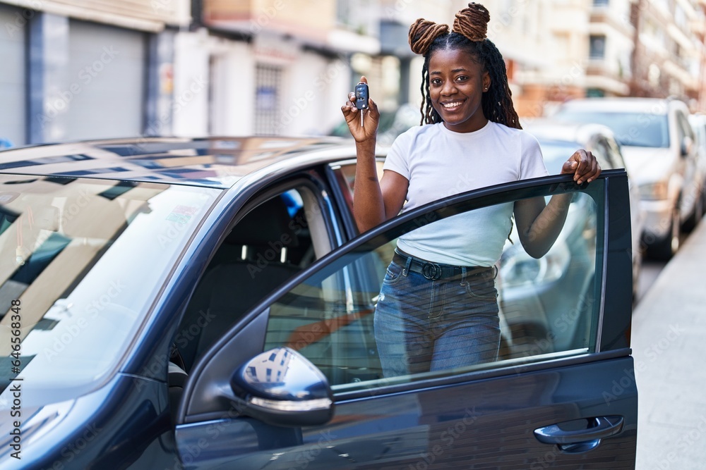 Naklejka premium African american woman smiling confident holding key of new car at street