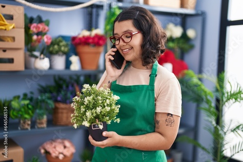 Young woman florist talking on smartphone holding plant pot at florist