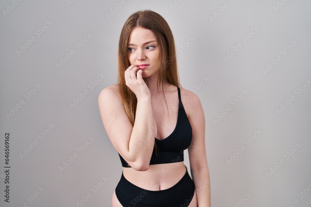 Young caucasian woman wearing lingerie looking stressed and nervous with hands on mouth biting nails. anxiety problem. Young caucasian woman wearing lingerie looking stressed and nervous with hands on mouth biting nails. anxiety problem.