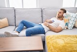 Young caucasian man listening to music lying on sofa at home