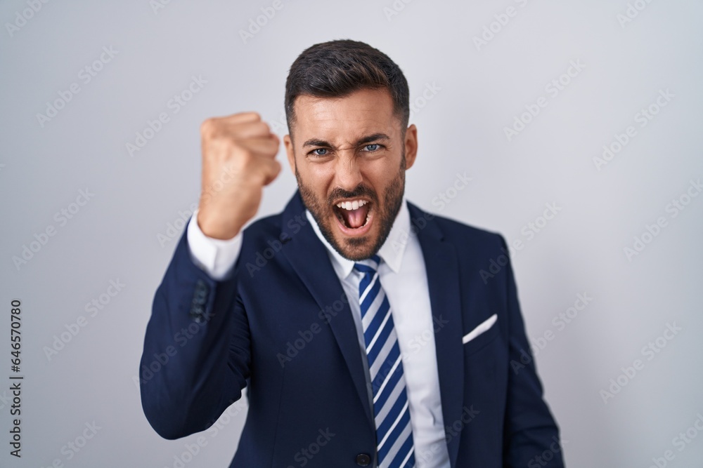 Handsome hispanic man wearing suit and tie angry and mad raising fist frustrated and furious while shouting with anger. rage and aggressive concept. Handsome hispanic man wearing suit and tie angry and mad raising fist frustrated and furious while shouting with anger. rage and aggressive concept.
