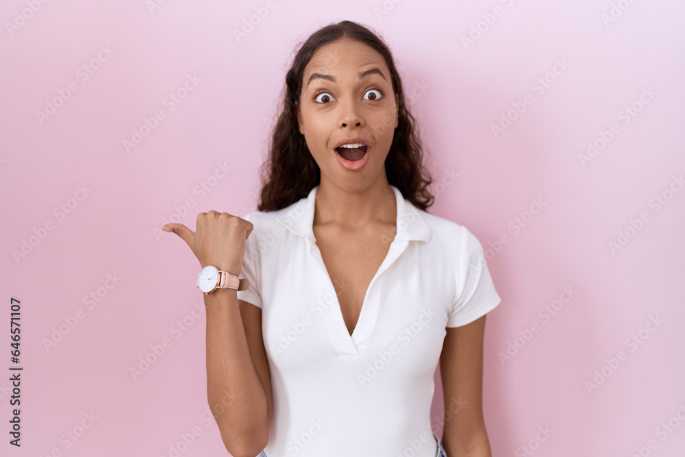 Young hispanic woman wearing casual white t shirt surprised pointing with hand finger to the side, open mouth amazed expression.