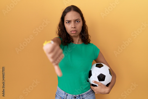 Young hispanic woman holding ball looking unhappy and angry showing rejection and negative with thumbs down gesture. bad expression. © Krakenimages.com