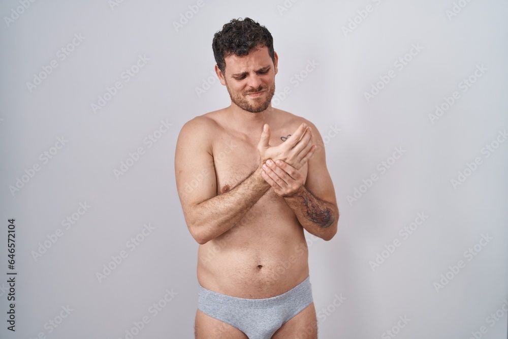 Young hispanic man standing shirtless wearing underware suffering pain on hands and fingers, arthritis inflammation