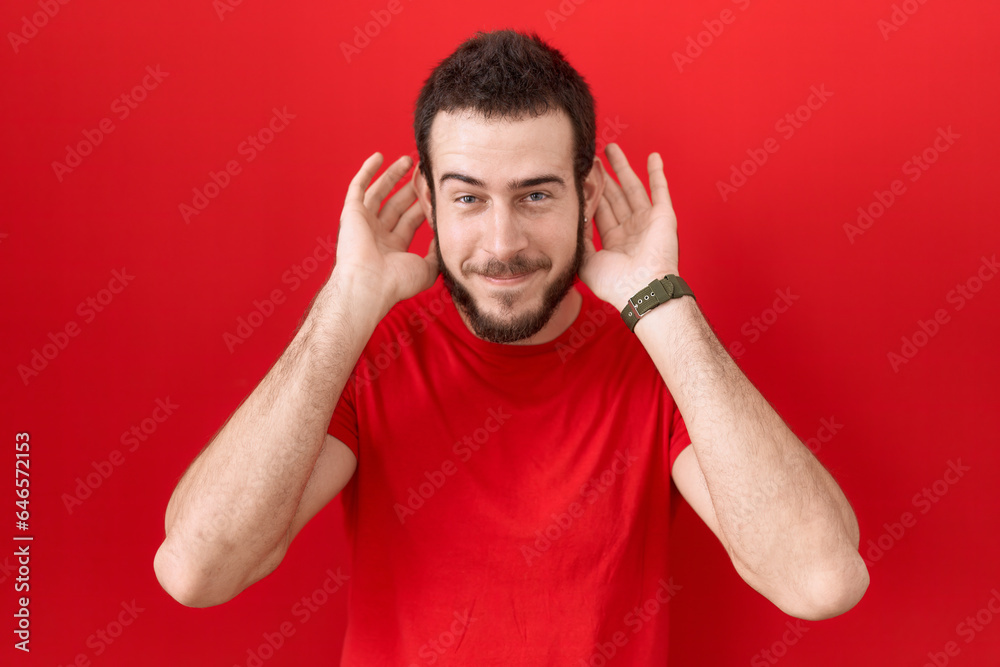 Young hispanic man wearing casual red t shirt trying to hear both hands on ear gesture, curious for gossip. hearing problem, deaf