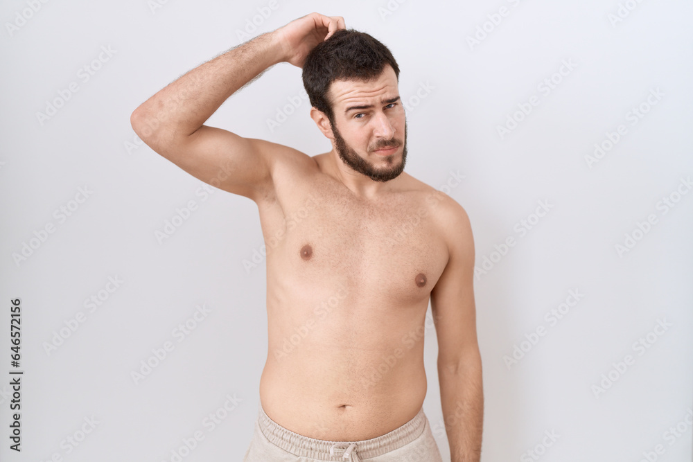 Young hispanic man standing shirtless over white background confuse and wonder about question. uncertain with doubt, thinking with hand on head. pensive concept.