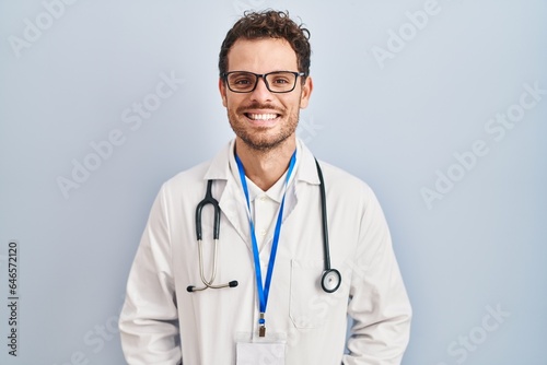 Young hispanic man wearing doctor uniform and stethoscope with a happy and cool smile on face. lucky person.
