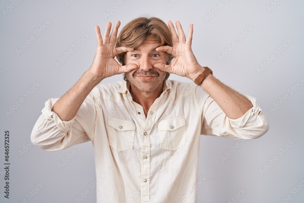 Middle age man standing over isolated background trying to open eyes with fingers, sleepy and tired for morning fatigue Middle age man standing over isolated background trying to open eyes with fingers, sleepy and tired for morning fatigue