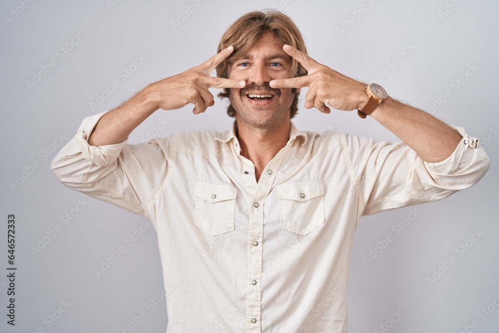 Middle age man standing over isolated background doing peace symbol with fingers over face, smiling cheerful showing victory Middle age man standing over isolated background doing peace symbol with fingers over face, smiling cheerful showing victory