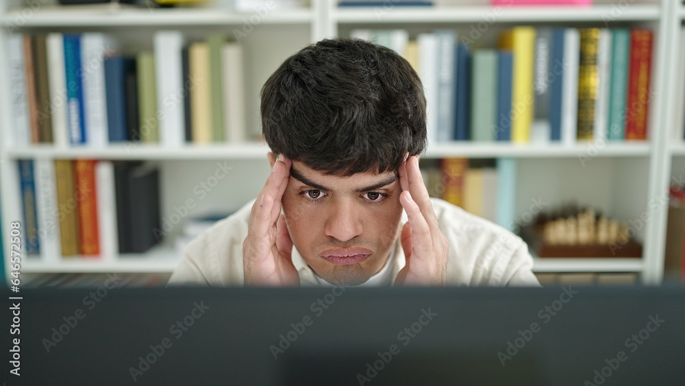 Young hispanic man student stressed using computer studying at library university