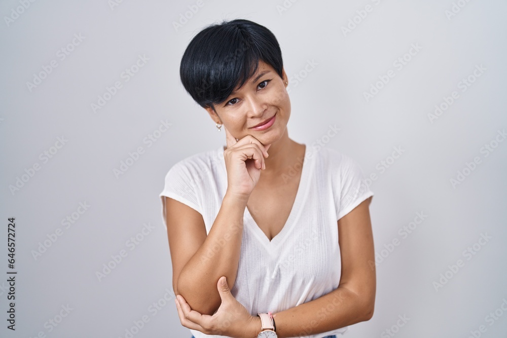 Young asian woman with short hair standing over isolated background looking confident at the camera smiling with crossed arms and hand raised on chin. thinking positive. Young asian woman with short hair standing over isolated background looking confident at the camera smiling with crossed arms and hand raised on chin. thinking positive.