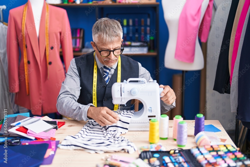 Middle age grey-haired man tailor using sewing machine at clothing factory