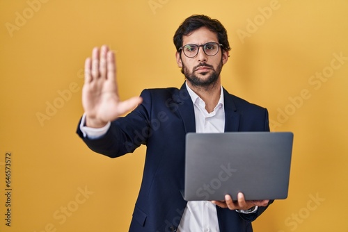 Handsome latin man working using computer laptop doing stop sing with palm of the hand. warning expression with negative and serious gesture on the face.