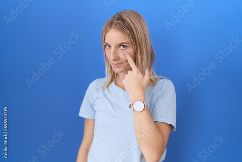 Young caucasian woman wearing casual blue t shirt pointing to the eye watching you gesture, suspicious expression