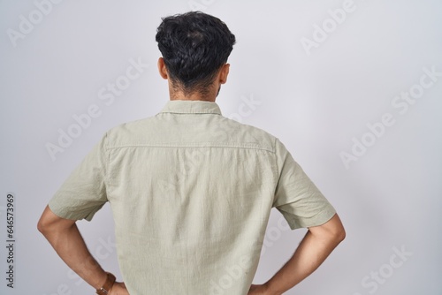 Arab man with beard standing over white background standing backwards looking away with arms on body