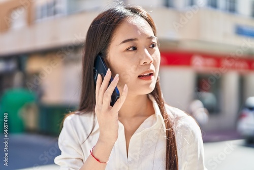 Young chinese woman talking on smartphone with serious expression at street