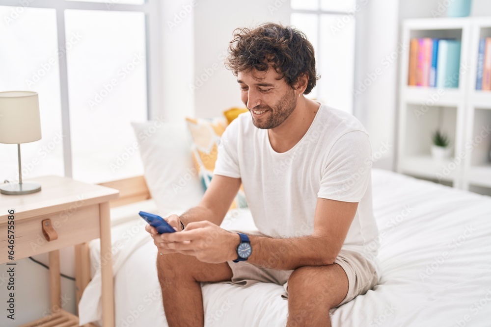 Young hispanic man using smartphone sitting on bed at bedroom Young hispanic man using smartphone sitting on bed at bedroom