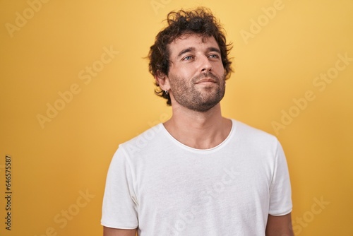 Young hispanic man standing looking to the side over isolated yellow background © Krakenimages.com