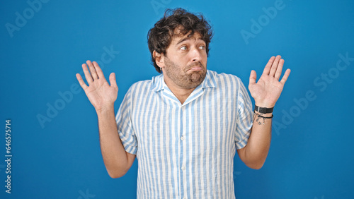 Obraz na płótnie Young hispanic man standing clueless over isolated blue background