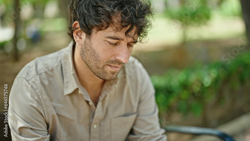 Young hispanic man sitting on bench with serious face at park