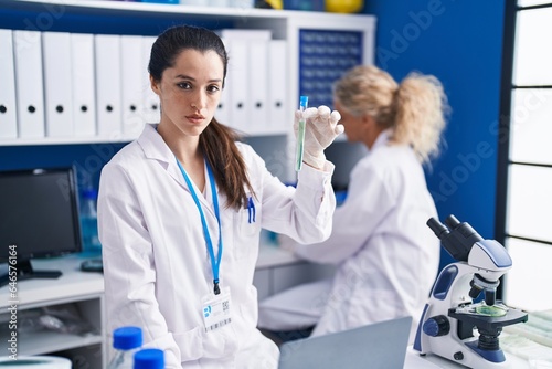 Young hispanic woman working at scientist laboratory thinking attitude and sober expression looking self confident