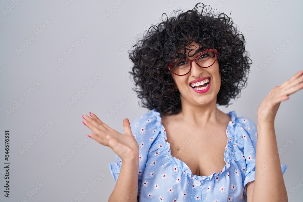 Young brunette woman with curly hair wearing glasses over isolated background celebrating crazy and amazed for success with arms raised and open eyes screaming excited. winner concept Young brunette woman with curly hair wearing glasses over isolated background celebrating crazy and amazed for success with arms raised and open eyes screaming excited. winner concept