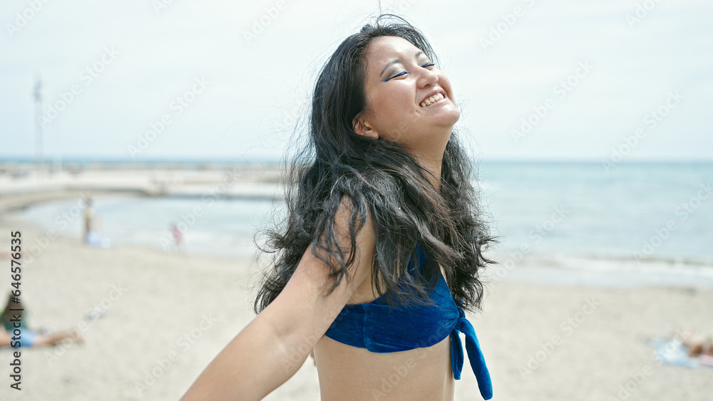 Young chinese woman tourist wearing bikini standing with open arms at the beach