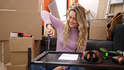 Young blonde woman repairing table using screwdriver at new home photo