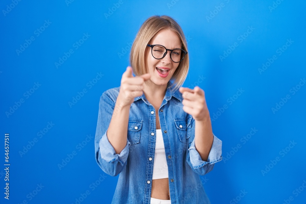 Young caucasian woman standing over blue background pointing fingers to camera with happy and funny face. good energy and vibes. Young caucasian woman standing over blue background pointing fingers to camera with happy and funny face. good energy and vibes.