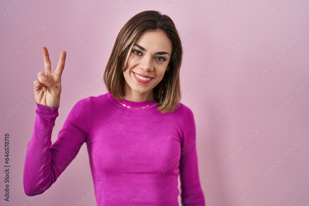 Hispanic woman standing over pink background showing and pointing up with fingers number two while smiling confident and happy. Hispanic woman standing over pink background showing and pointing up with fingers number two while smiling confident and happy.