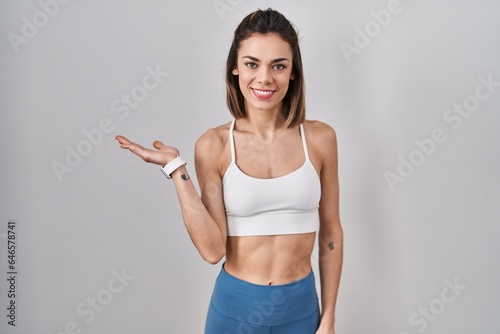 Hispanic woman wearing sportswear over isolated background smiling cheerful presenting and pointing with palm of hand looking at the camera. © Krakenimages.com