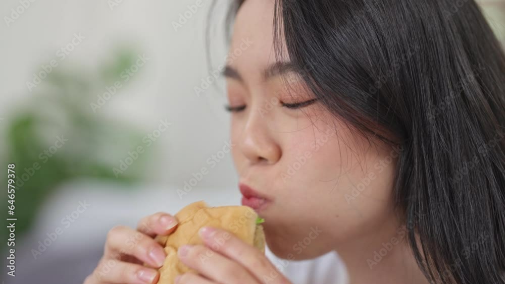 Close up young woman eating burger at home. Close up young woman eating burger at home.