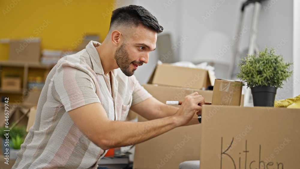 Young hispanic man smiling confident writing on package at new home Young hispanic man smiling confident writing on package at new home